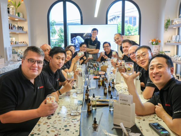 b2b workshop. Group of coworkers in black shirts raise beverage samples around a long table in a bright retail space, smiling for the photo.