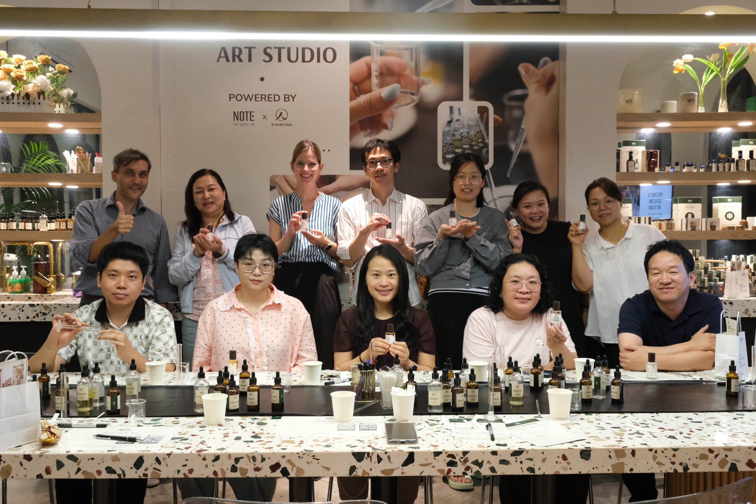 Group of people in an art studio posing behind a table filled with small bottles and droppers on a terrazzo surface.