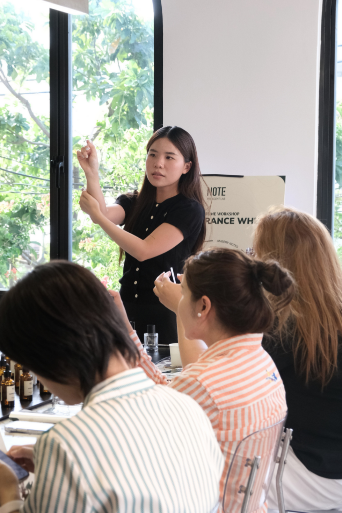 Female presenter showing a small item to a group during a workshop, bottles lined up on the table.