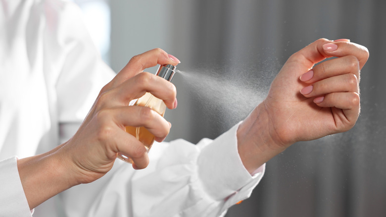 Close-up of a person spraying perfume onto their wrist from a bottle